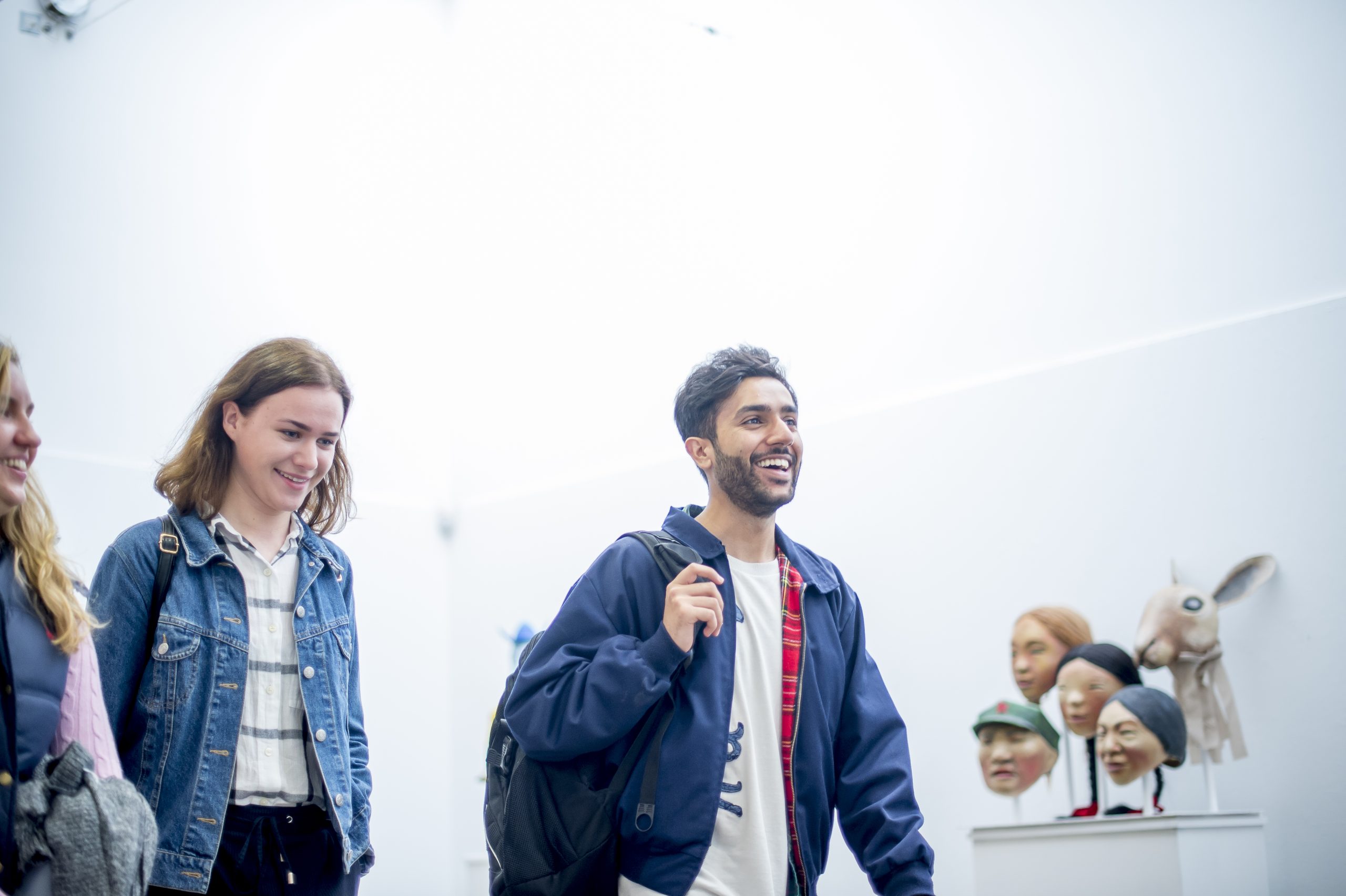 A student intern with long brown hair uses her phone to take a photo of a painting in a gallery