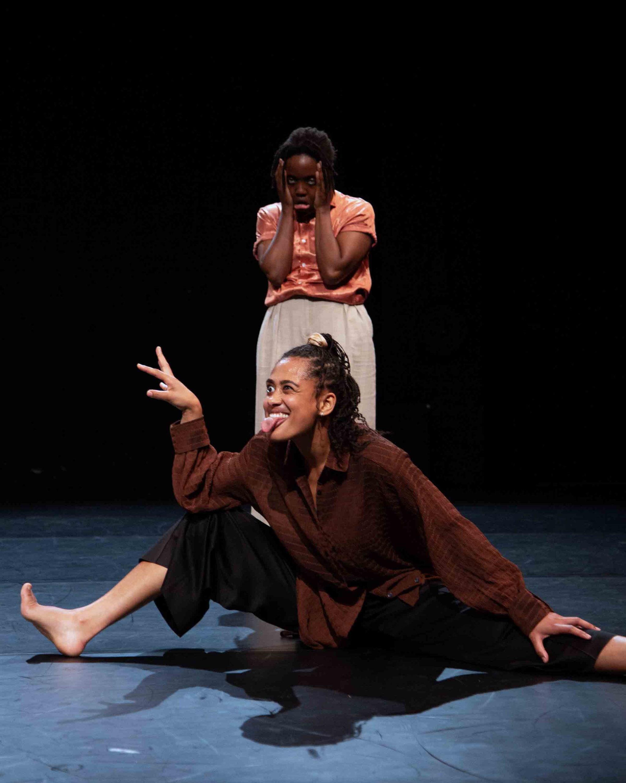 A woman stands with her head in her hands whilst another pulls a mischievous face