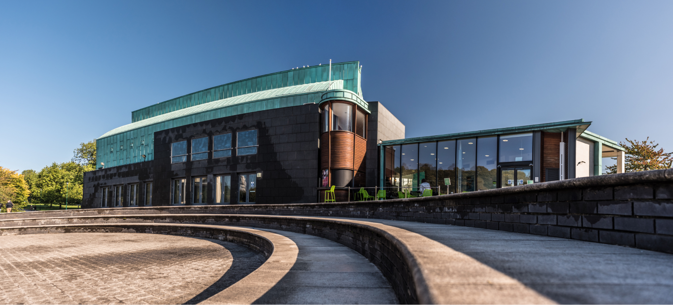 A building with a green roof and large windows sat next to a lake