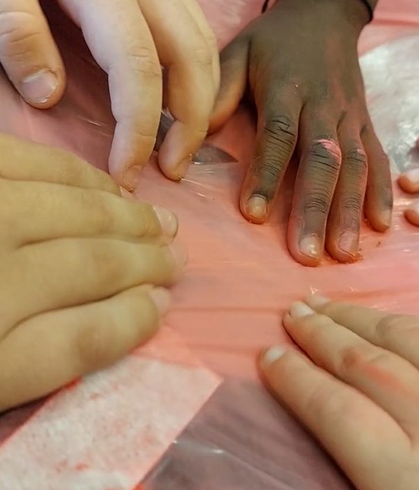 Children place their hands on a piece of cellophane stretched over a speaker
