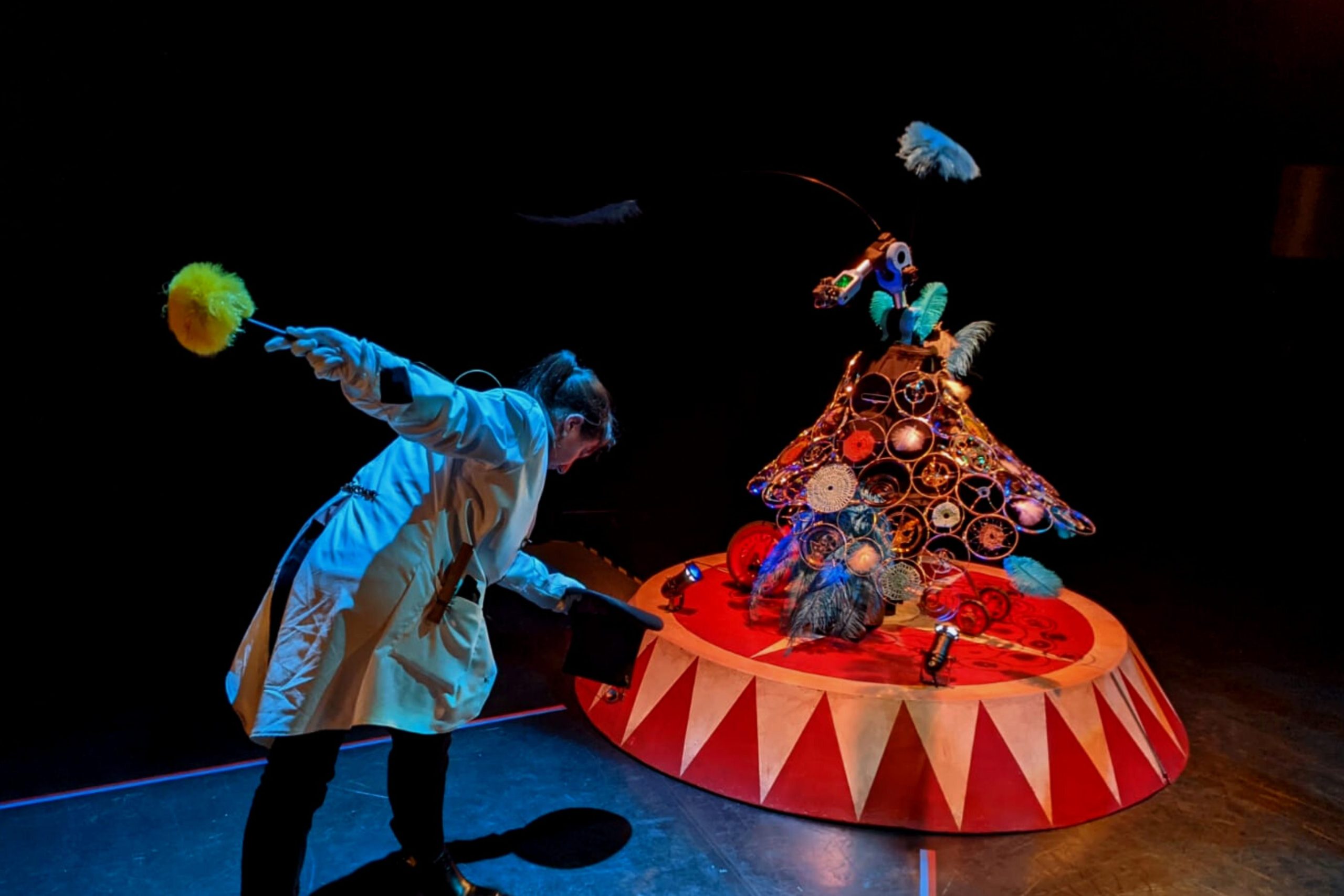A woman in a la coat bends to press a button on a contraption that looks like a spinning circus performer