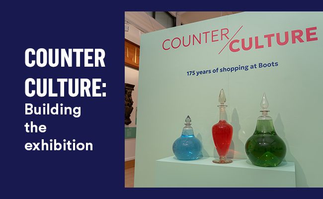 Three glass carboys sit in front of a pale green wall.