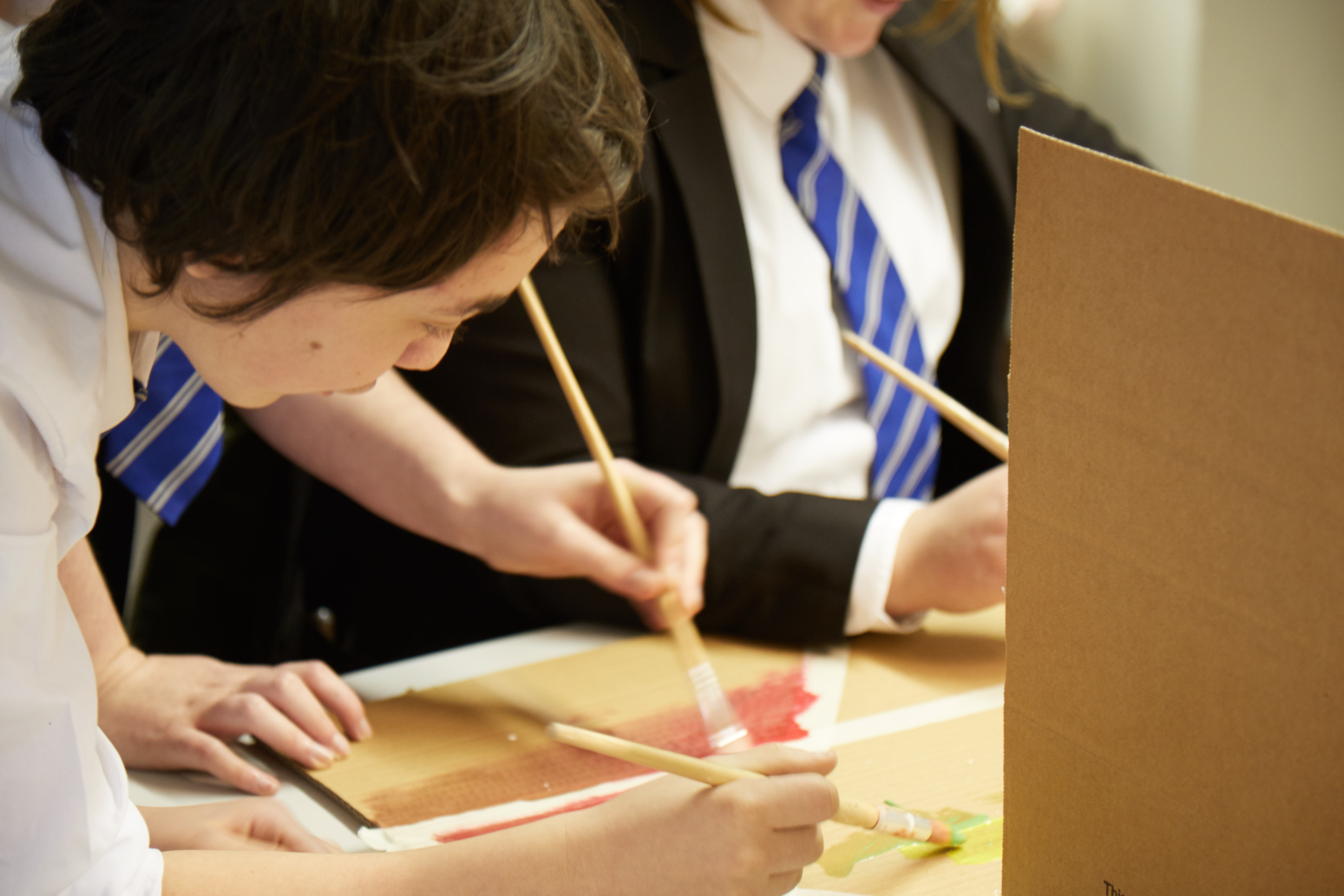 Two secondary school students in uniform painting in yellows, reds and oranges as part of a school trip at Lakeside Arts.