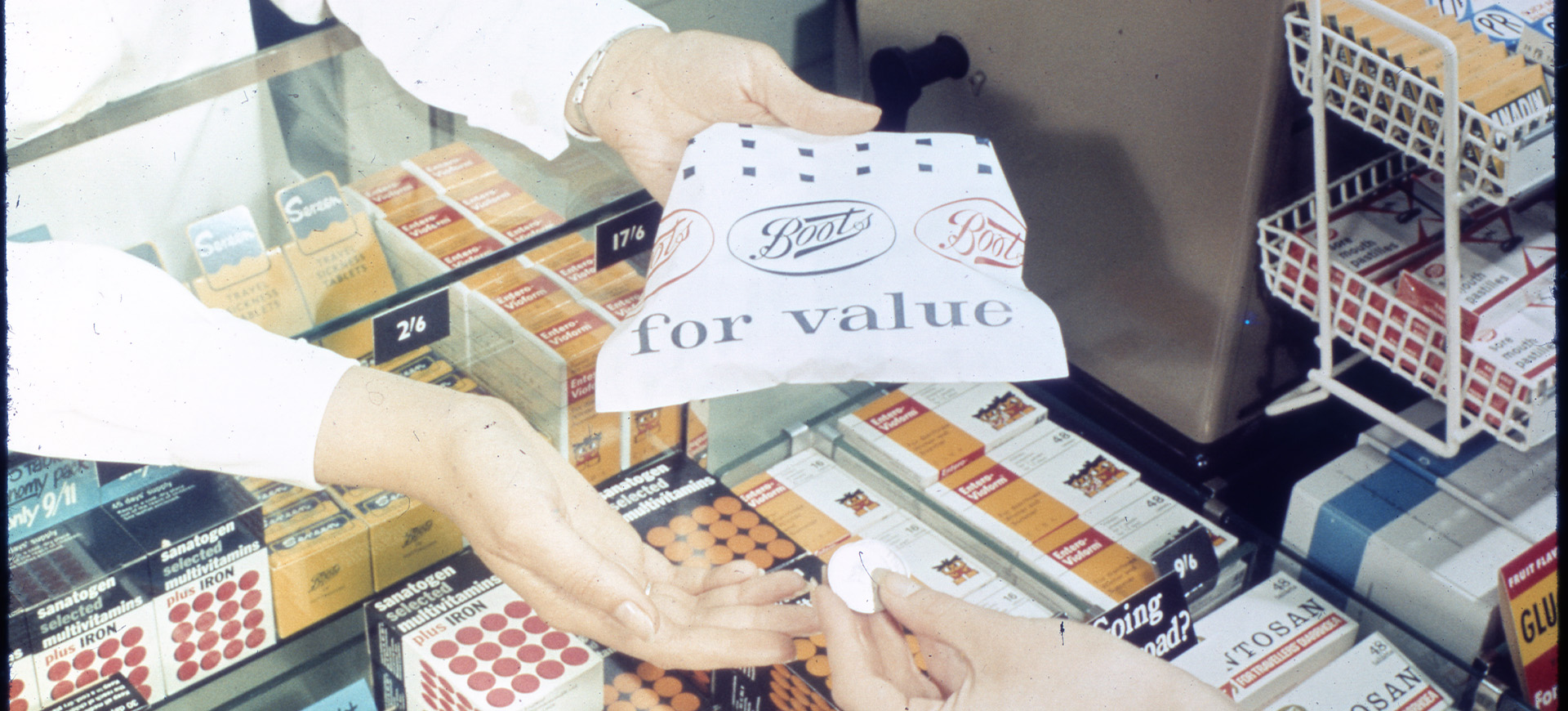 A woman handing a Boots paper bag to a customer over a pharmacy counter