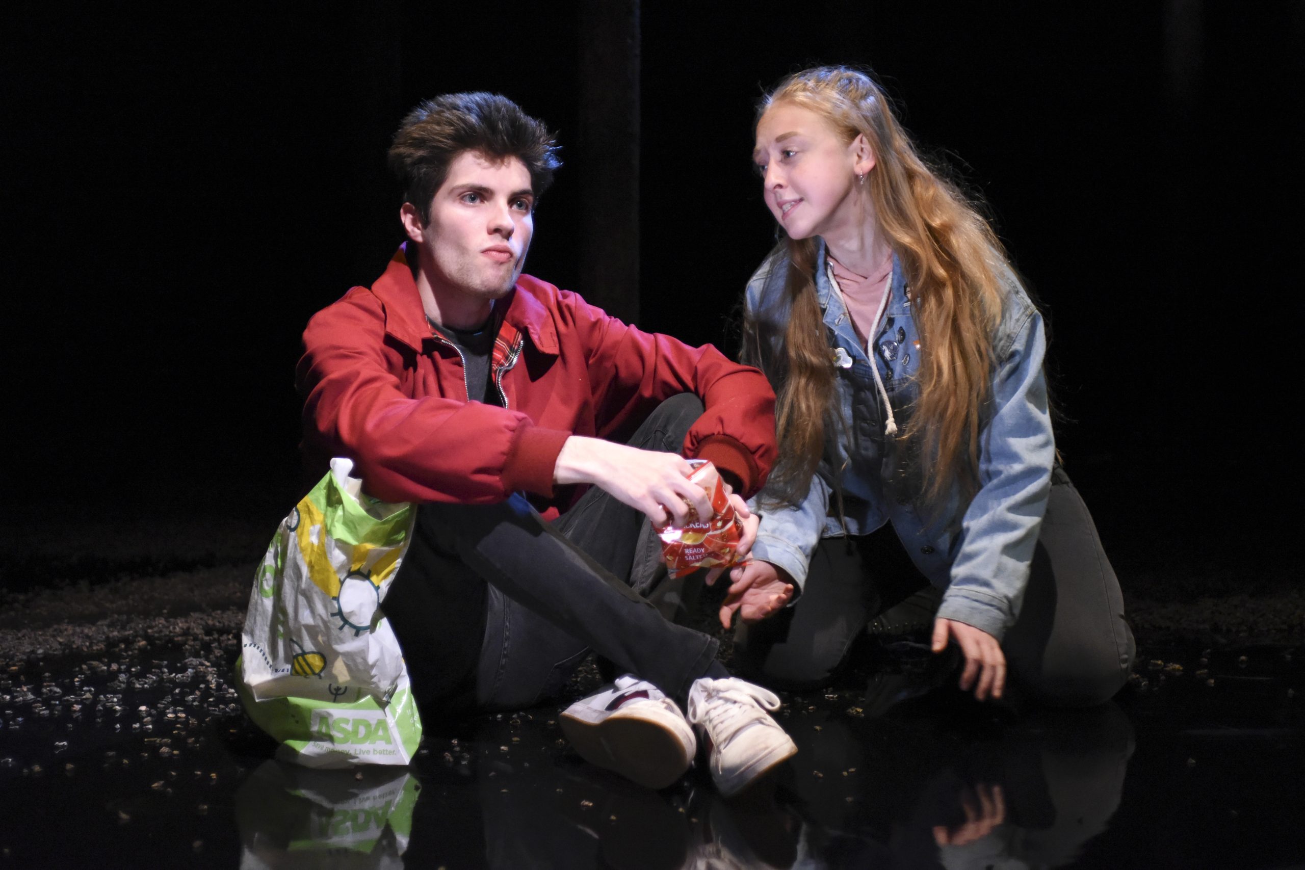 a man in a red shirt looks unimpressed as a girl tries to get his attention