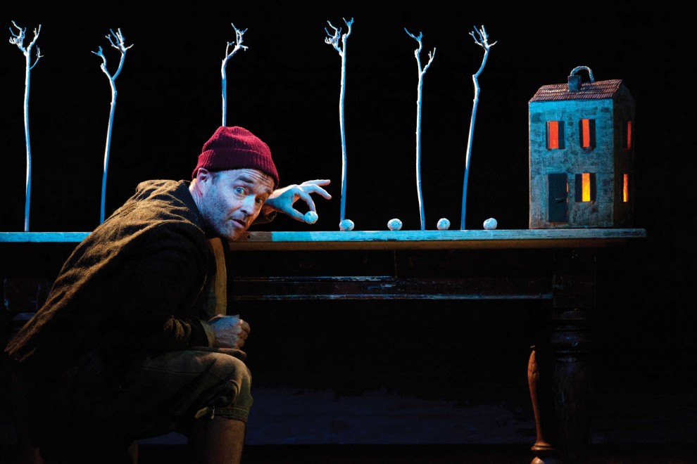 A man in a red hat runs his hand on a table with a lit up house