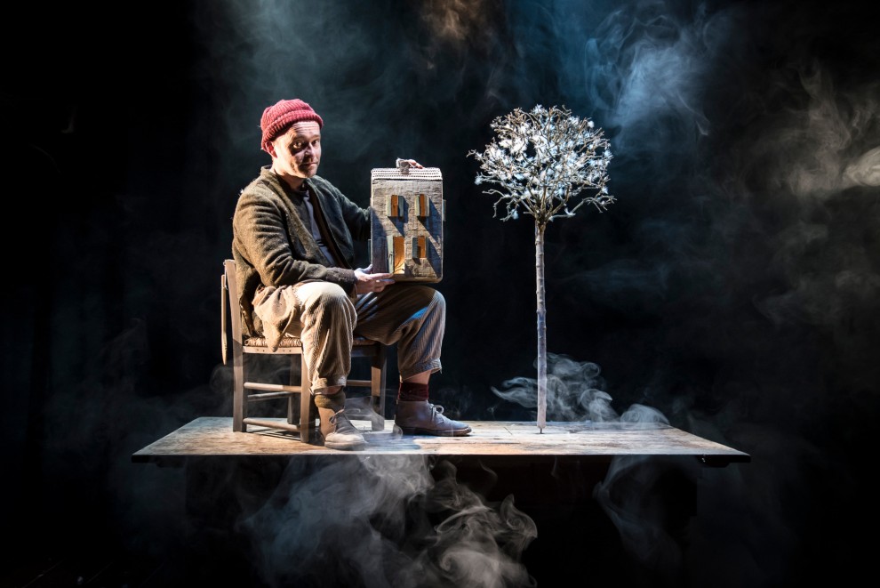 A man in a red hat sits on a table with a tree made of feathers
