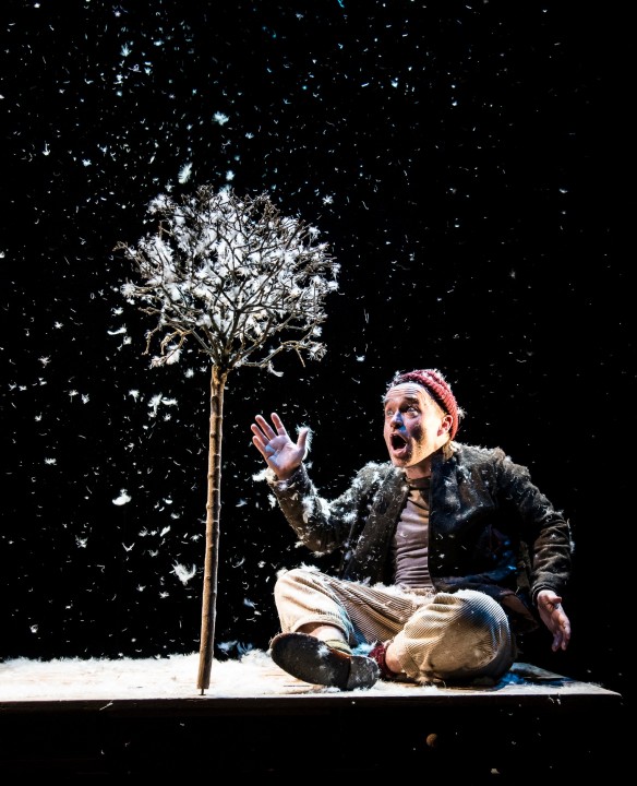 A man sits on stage with a tree made of feathers