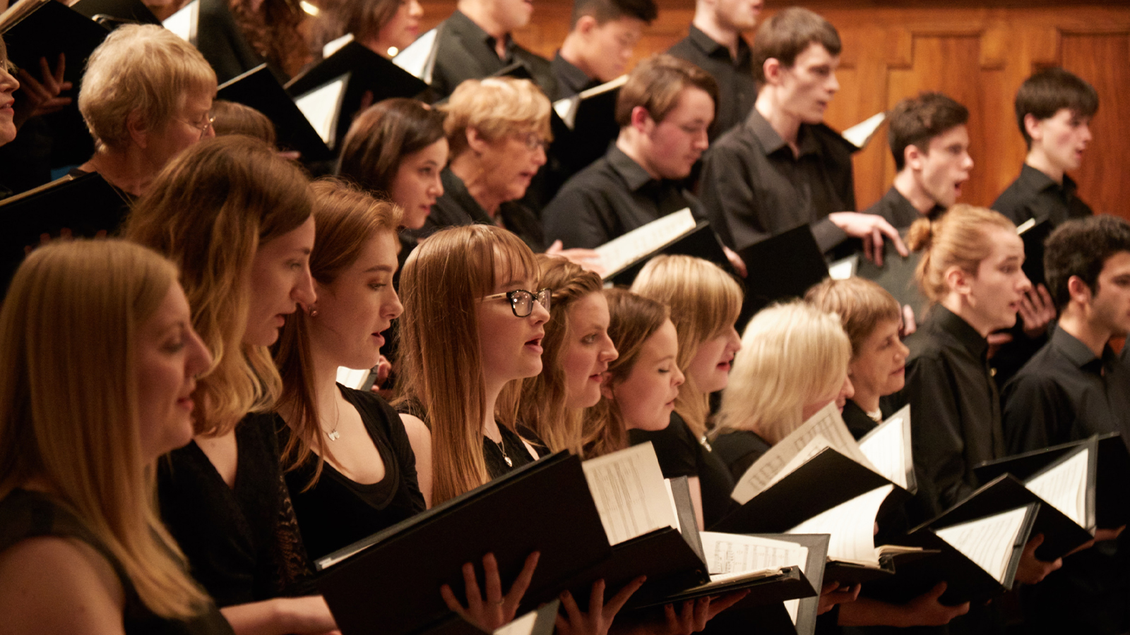 a choir all dressed in black sing whilst holding sheet music