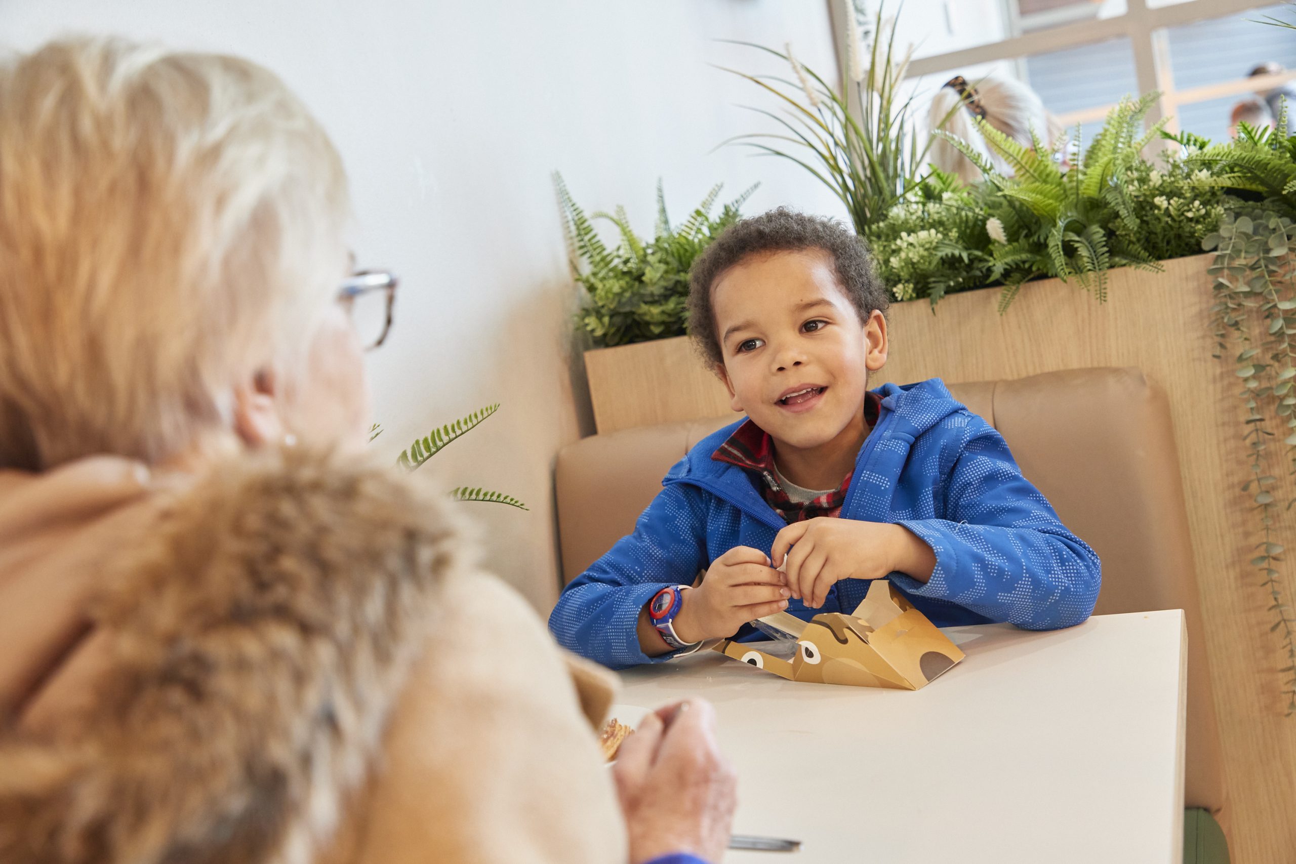 A small boy in a blue hoodie sits at a cafe table