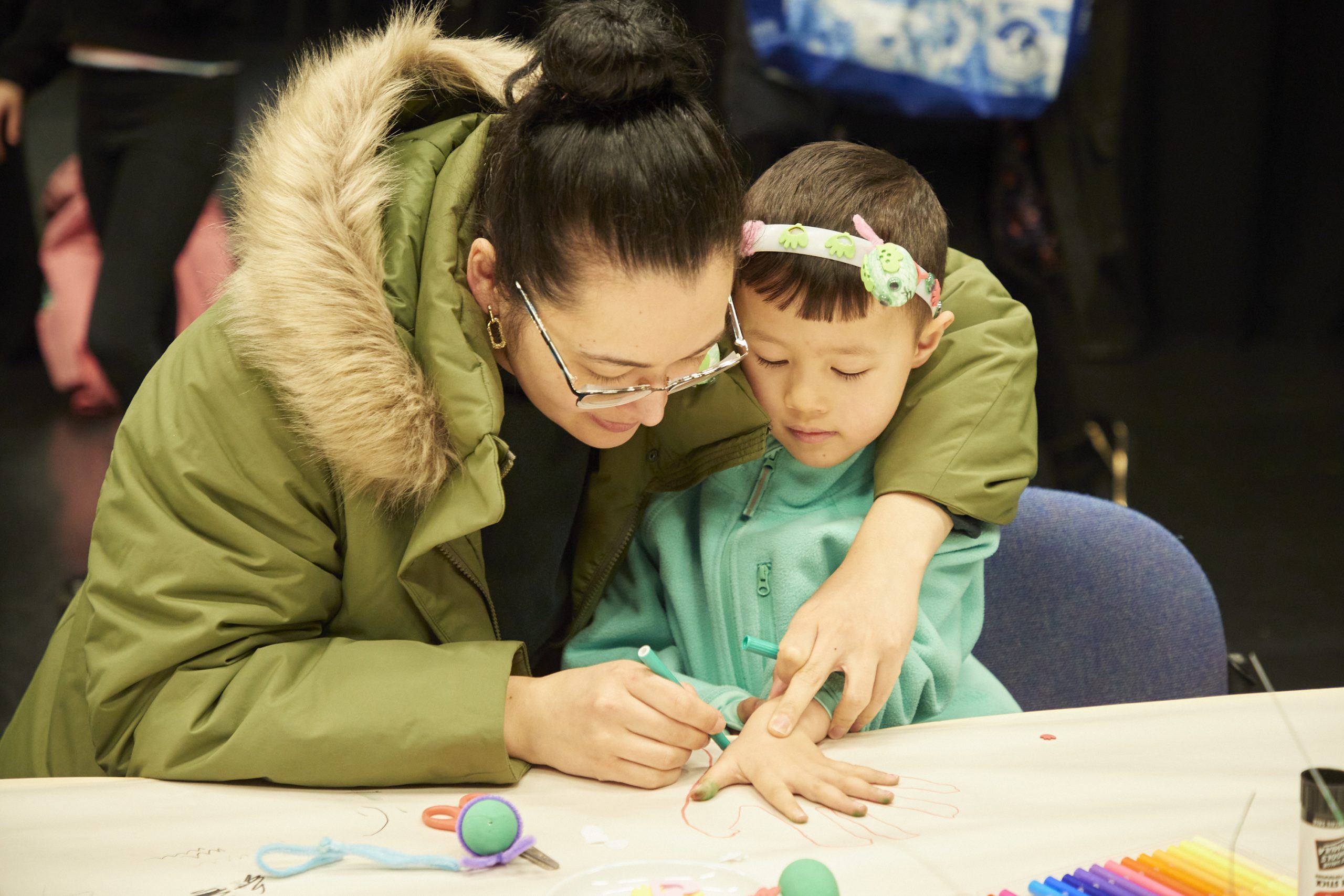 A mother and child smile as they make a craft headband