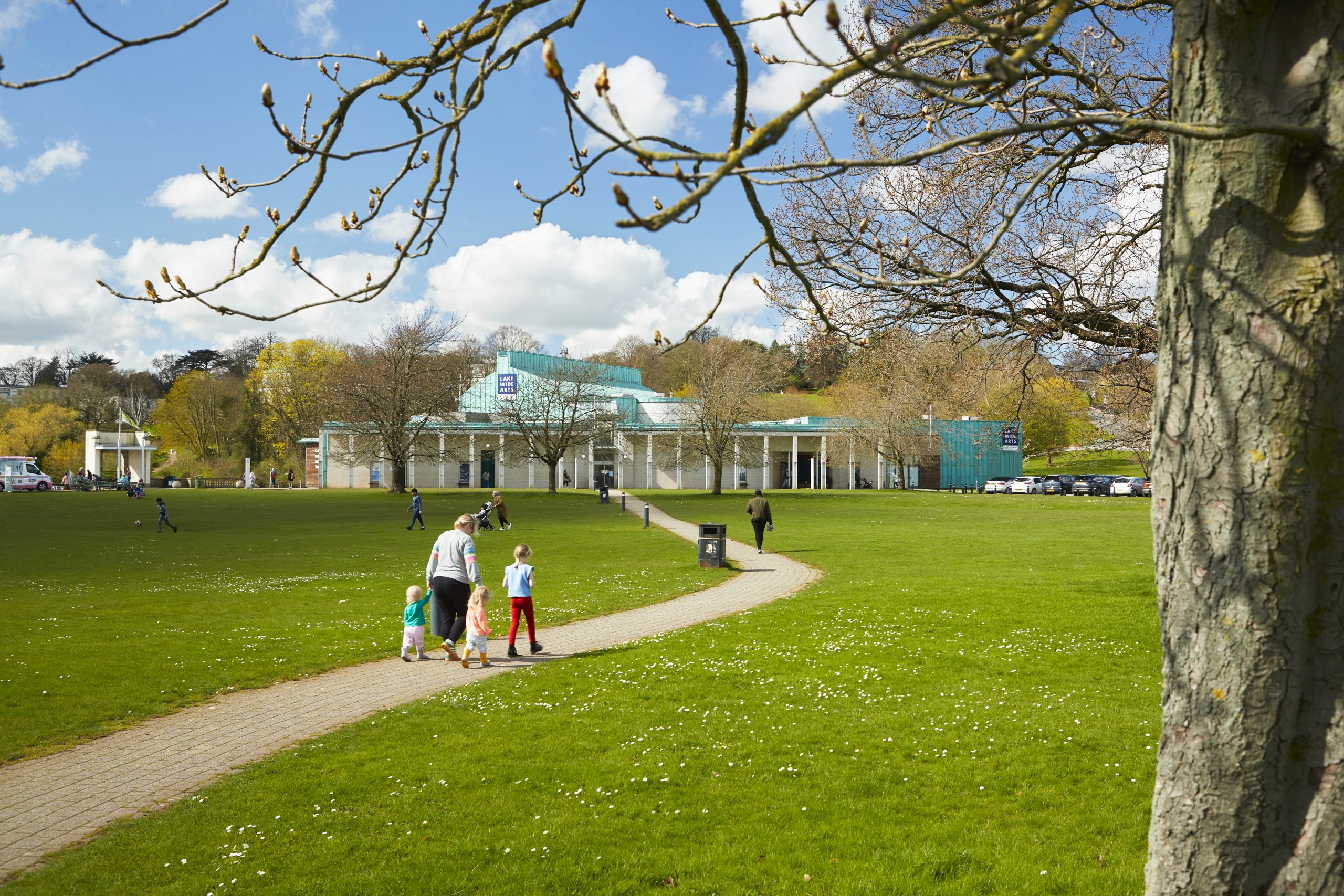 A family walk along a park path towards Lakeside Arts