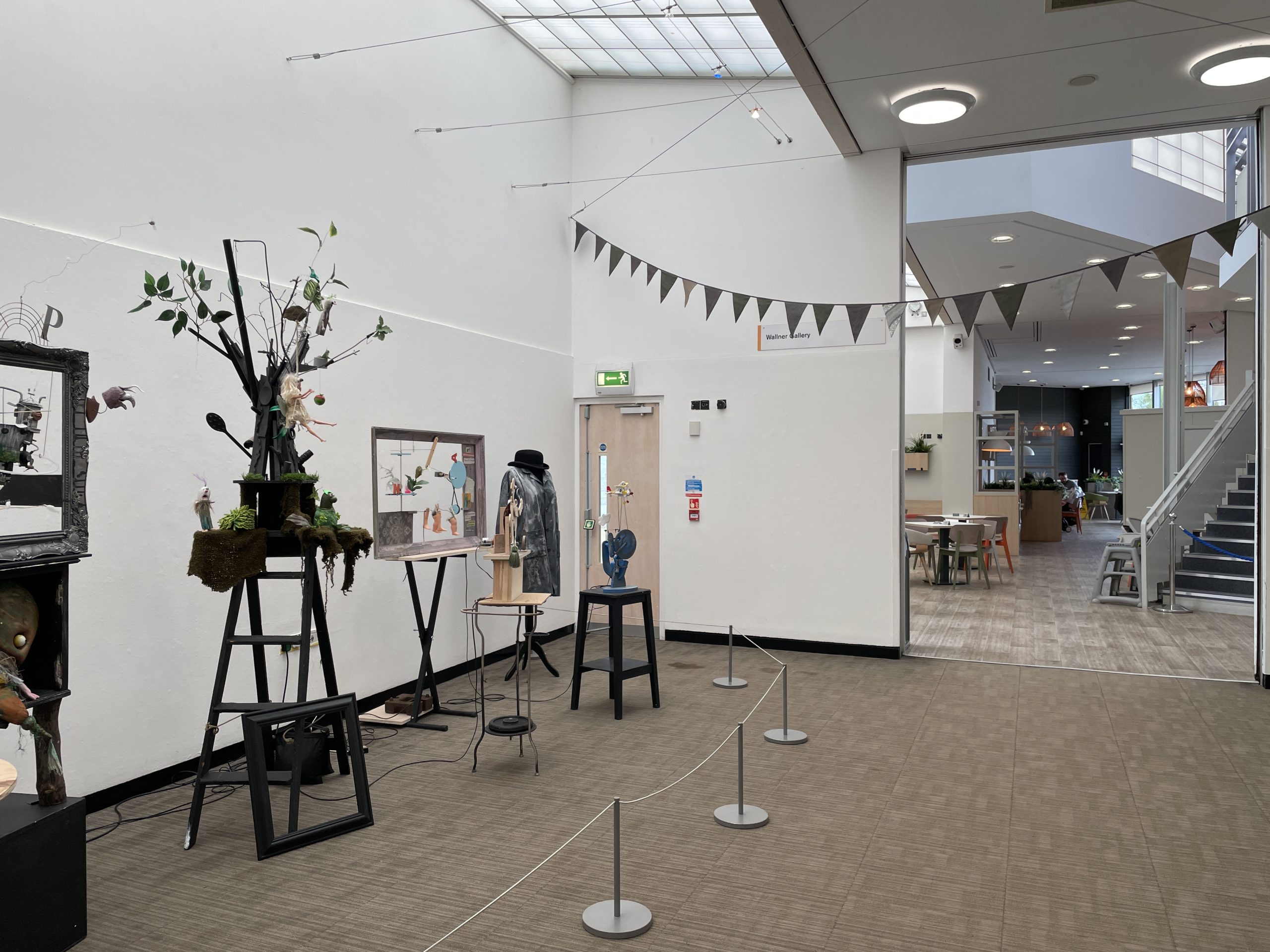 A puppet exhibition sits in a white gallery space, with cafe area in the background.